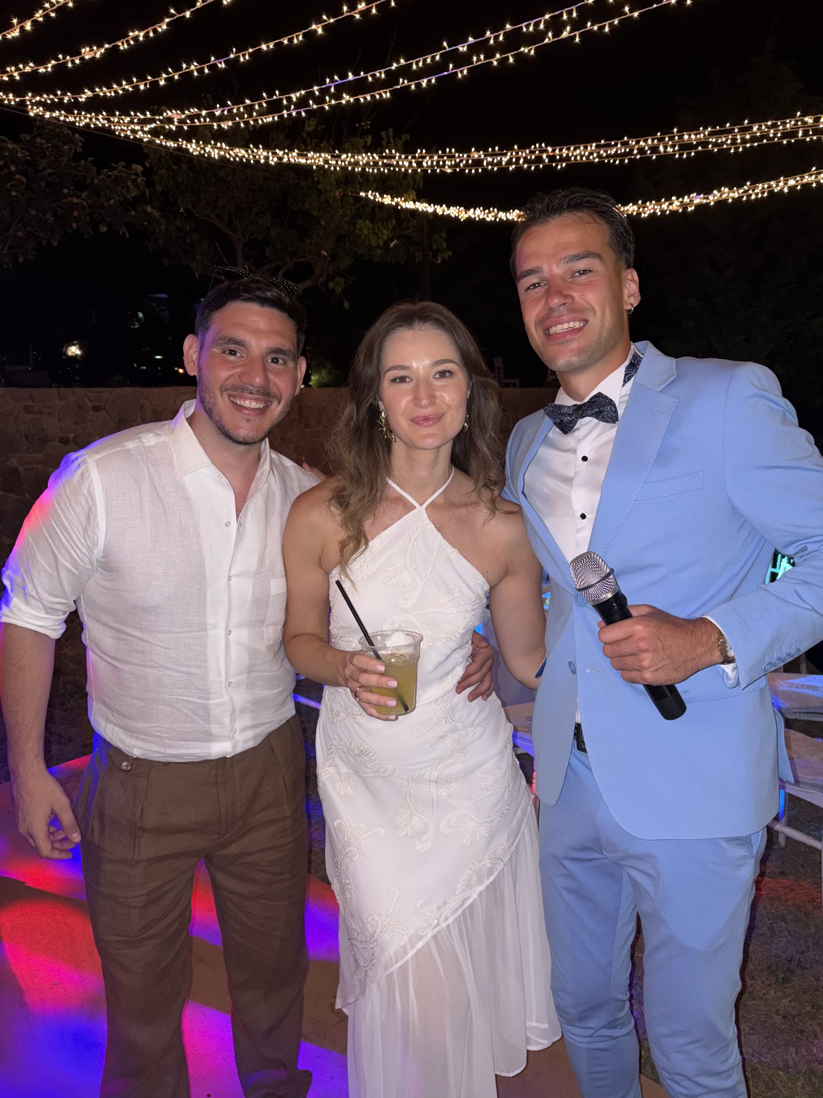 Vova with Alyona and Lampros beneath lights at their wedding in Greece