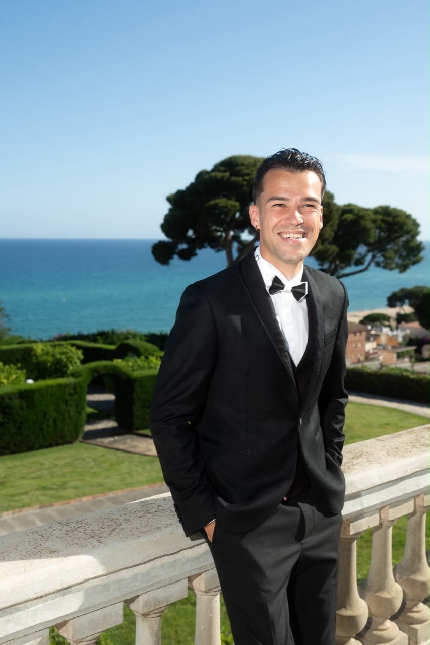Vova smiling in a black tuxedo with the sea behind him