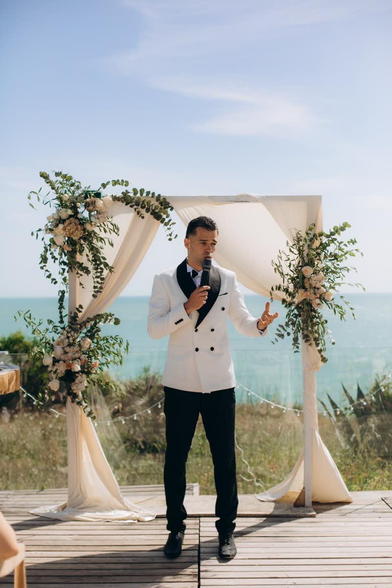 Vova leading a wedding ceremony beneath a flower arch overlooking the sea