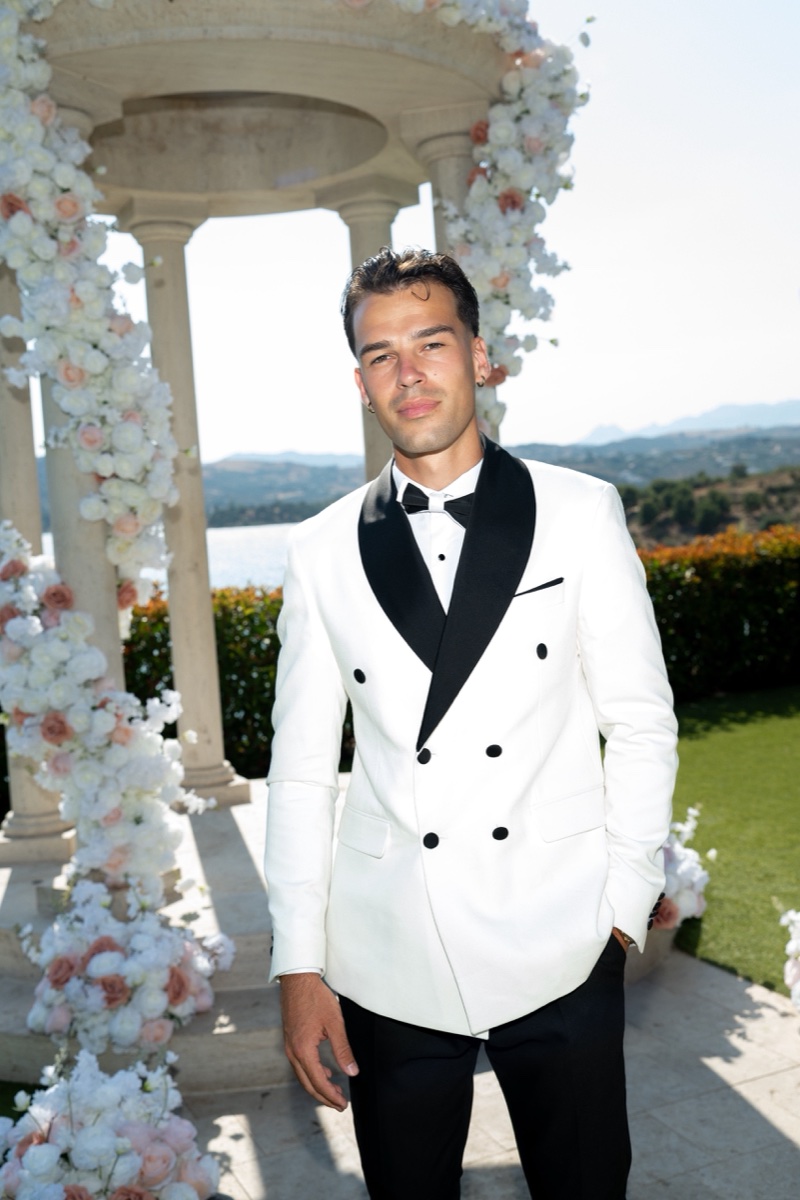 Vova in a white dinner jacket beside the wedding's floral arch